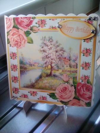 Pretty woodland with cottage and stream with pink/peach roses 8x8 by Joyce Edwards