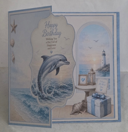 Coastal Dolphin Birthday Card Front – Ocean Sunset, Lighthouse & Seashell Design by Marion Harding
